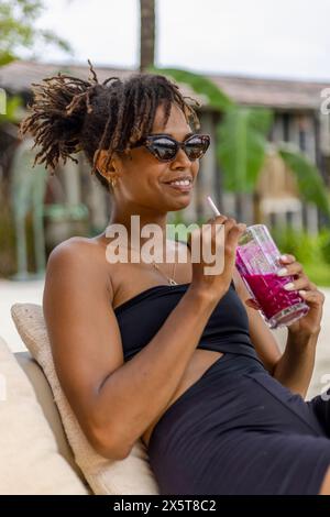 Lächelnde Frau im Badeanzug, die Smoothie auf der Terrasse trinkt Stockfoto