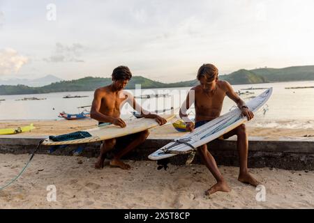 Indonesien, Lombok, Surfer bereiten Surfbretter am Strand bei Sonnenuntergang vor Stockfoto