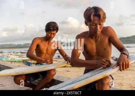 Indonesien, Lombok, Surfer bereiten Surfbretter am Strand bei Sonnenuntergang vor Stockfoto