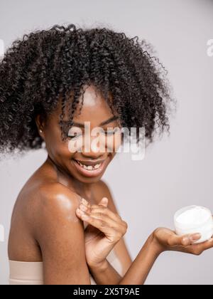 Studio-Porträt einer lächelnden Frau, die Feuchtigkeitspflege auf den Arm aufträgt Stockfoto
