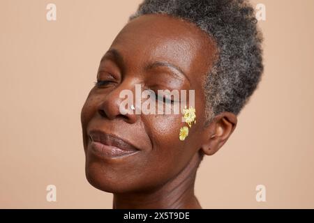 Porträt einer lächelnden Seniorin mit geschlossenen Augen vor beigefarbenem Hintergrund Stockfoto