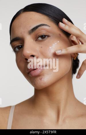 Studio-Aufnahme einer jungen Frau, die Creme auf das Gesicht aufträgt Stockfoto