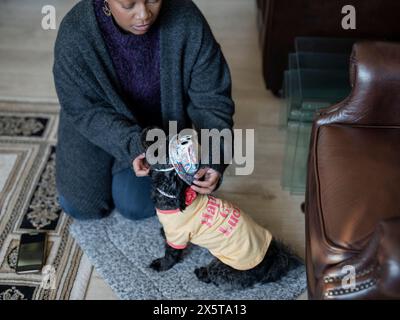 Frau, die Shih Tzu Poodle verkleidet, während sie zu Hause auf Teppich sitzt Stockfoto