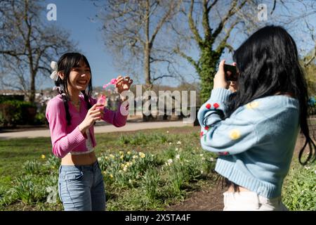 Junge Frau, die einen Freund aufnimmt, der Blasen im Park bläst Stockfoto