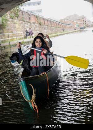 Zwei junge Frauen und Hund im Kanu auf dem Kanal Stockfoto