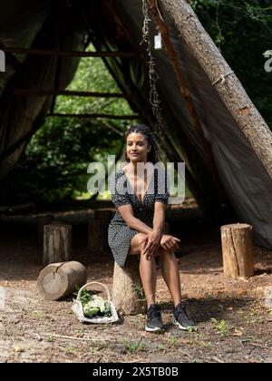 Frau, die auf Baumstumpf vor der Hütte im Wald ruht Stockfoto