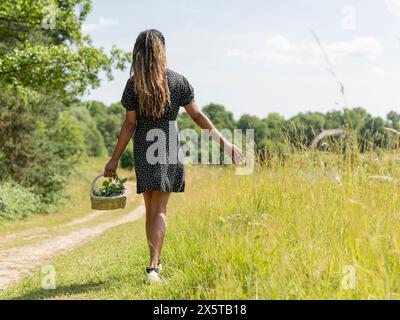 Frau mit Korb, die an sonnigem Tag durch die Wiese geht Stockfoto