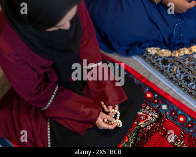 Frau kniend und hält Gebetskerlen während des Ramadan-Gebets zu Hause Stockfoto