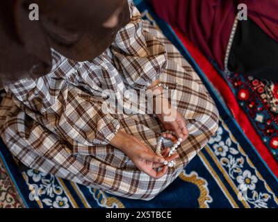Frau kniend und hält Gebetskerlen während des Ramadan-Gebets zu Hause Stockfoto