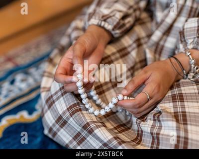 Frau, die während des Ramadan-Gebets zu Hause Gebetsperlen hält Stockfoto