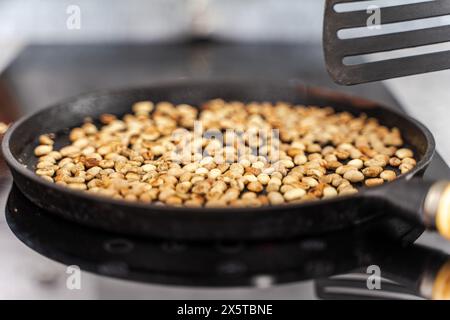 Der köstlichste Kaffee wird durch Rösten von Kaffeebohnen in einer Pfanne auf dem Herd gewonnen. Kaffeebohnen werden in einer gusseisernen Pfanne geröstet. Wählen Sie Aus Stockfoto