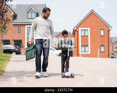 Junge (6-7) auf dem Roller, der mit Vater zur Schule geht Stockfoto