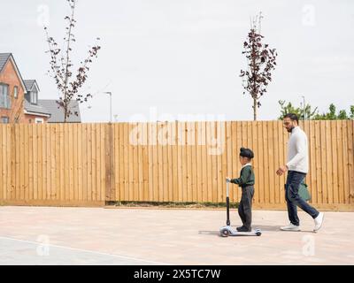 Junge (6-7) auf dem Roller, der mit Vater zur Schule geht Stockfoto