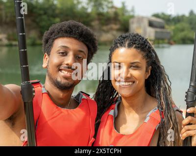 Porträt lächelnder Freunde, die Schwimmwesten tragen und Ruder halten Stockfoto