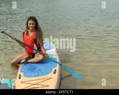 Lächelnde Frau, die auf dem Paddleboard auf dem See sitzt Stockfoto