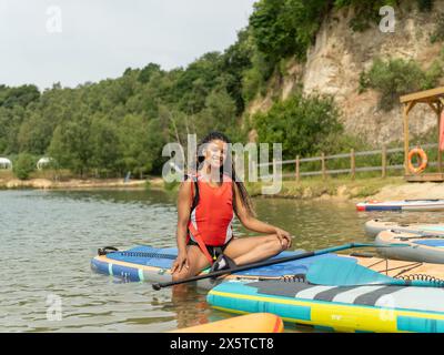 Lächelnde Frau, die auf dem Paddleboard auf dem See sitzt Stockfoto