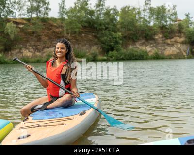 Lächelnde Frau, die auf dem Paddleboard auf dem See sitzt Stockfoto