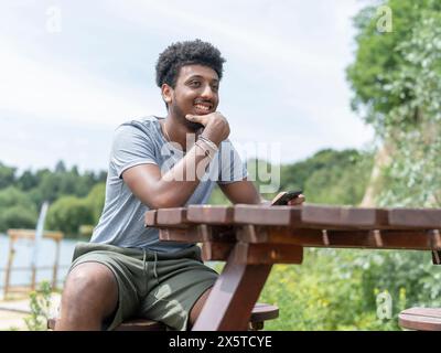 Junger Mann, der am See sitzt Stockfoto