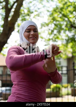 UK, Sutton, lächelnde Frau im Kopftuch, die Smartwatch überprüft Stockfoto