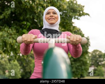 UK, Sutton, lächelnde Frau im Kopftuch, die im Park Gym trainiert Stockfoto