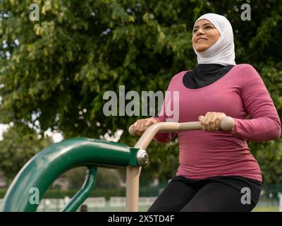 UK, Sutton, lächelnde Frau im Kopftuch, die im Park Gym trainiert Stockfoto