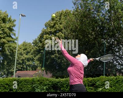 Großbritannien, Sutton, Frau im Kopftuch, die Tennis im Park spielt Stockfoto