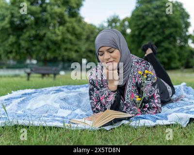 Großbritannien, Sutton, Frau im Kopftuch, die Buch auf dem Rasen im Park liest Stockfoto