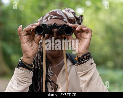 Lächelnde Wanderer, die durch das Fernglas im Wald schaut Stockfoto