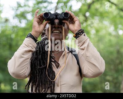 Lächelnde Wanderer, die durch das Fernglas im Wald schaut Stockfoto