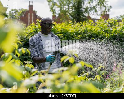 Lächelnder reifer Mann, der Pflanzen im Garten tränkt Stockfoto