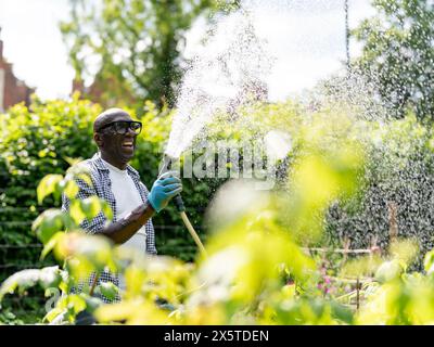 Lächelnder reifer Mann, der Pflanzen im Garten tränkt Stockfoto