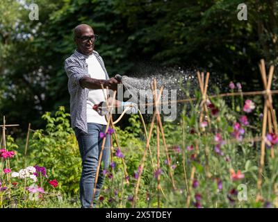 Lächelnder reifer Mann, der Pflanzen im Garten tränkt Stockfoto