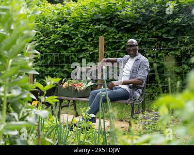 Ein lächelnder reifer Mann, der sich nach der Gartenarbeit auf der Bank ruht Stockfoto