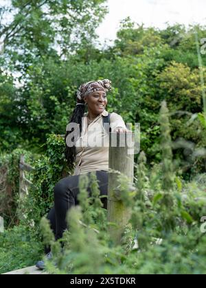 Lächelnde reife Frau, die auf einem Zaun auf der Wanderung sitzt Stockfoto