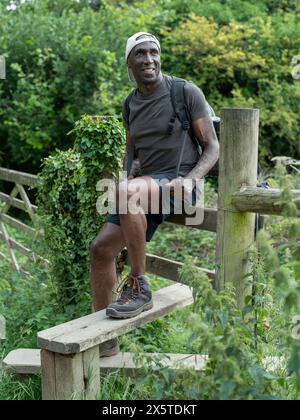 Lächelnder reifer Mann, der auf einem Zaun auf der Wanderung sitzt Stockfoto