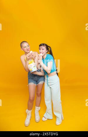 Studio-Porträt lächelnder, stilvoller Freunde, die Zuckerwatte essen Stockfoto