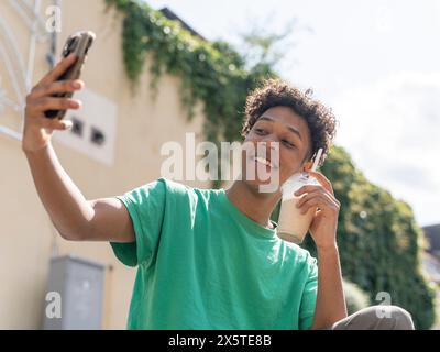 Junger Mann, der Selfie mit Smoothie an sonnigen Tagen macht Stockfoto