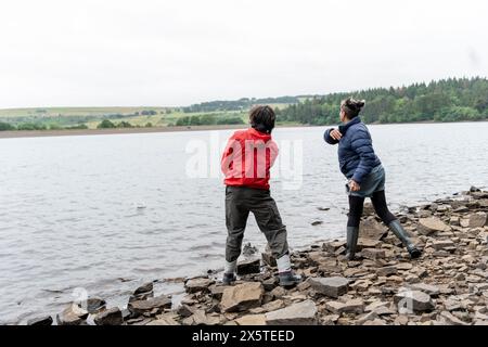 Mutter und Sohn überspringen Steine im See Stockfoto