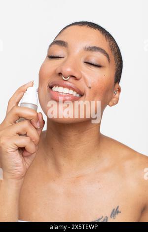 Studio-Porträt einer lächelnden Frau, die Gesichtsserum aufträgt Stockfoto