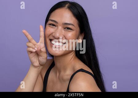 Lächelnde Frau, die in die Kamera schaut und Friedenszeichen macht Stockfoto