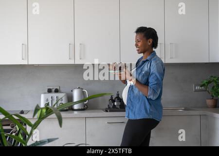 Lächelnde schwangere Frau, die in der Küche Teller mit roten Trauben hält Stockfoto