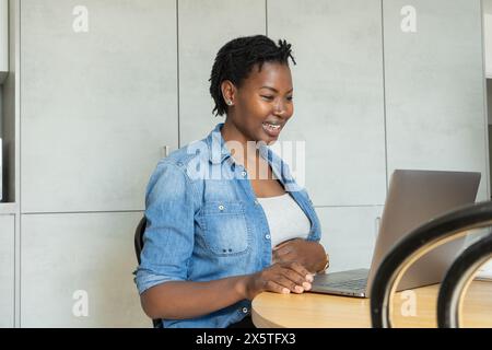 Lächelnde schwangere Frau mit Laptop in der Küche Stockfoto