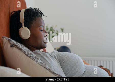 Schwangere Frau mit Kopfhörern, die sich im Bett entspannen Stockfoto