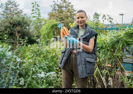 Porträt einer lächelnden Frau, die im städtischen Garten Karotten hält Stockfoto