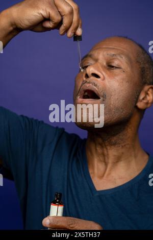 Mann, der Medikamente mit Pipette vor violettem Hintergrund einnimmt Stockfoto