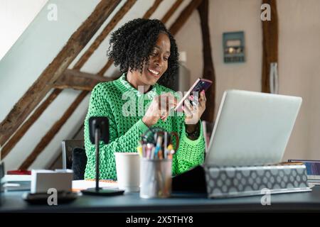 Lächelnde Geschäftsfrau mit Smartphone am Schreibtisch im Büro Stockfoto