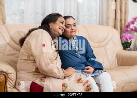 Porträt einer Frau, die mit Down-Syndrom-Enkelin im Wohnzimmer sitzt Stockfoto