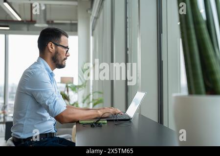 Geschäftsmann mit Laptop, der in einem modernen Büro arbeitet Stockfoto