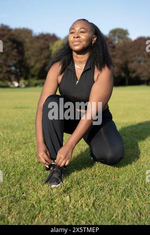 Junge Frau, die Schuhe bindet, bevor sie im Park trainiert Stockfoto