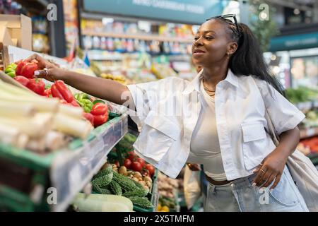 Eine junge Frau, die frisches Gemüse im Supermarkt wählt Stockfoto